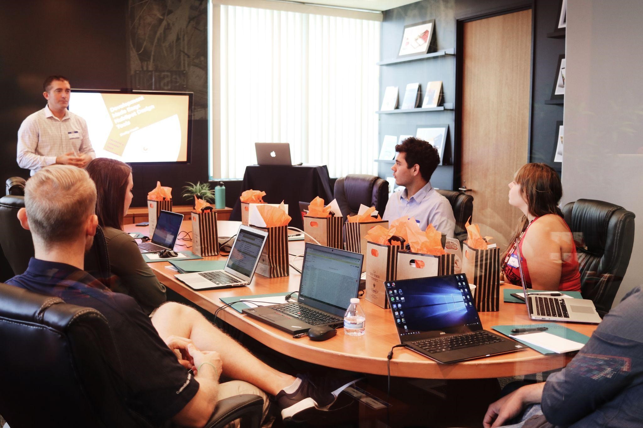 Image of a man standing in front of people sitting next to the table with laptops.