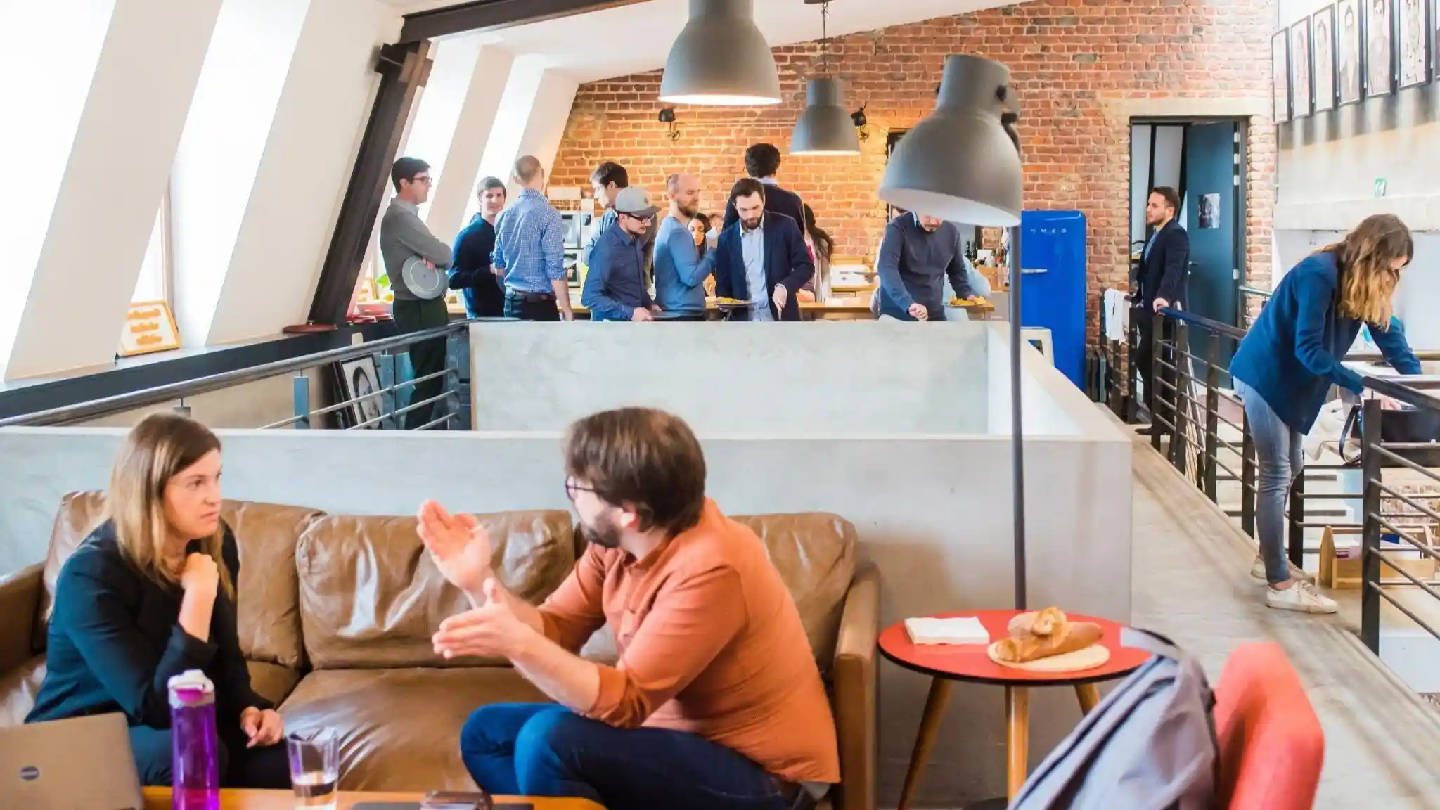 Image of a man in orange dress shirt talking and sitting in front of woman on brown sofa.